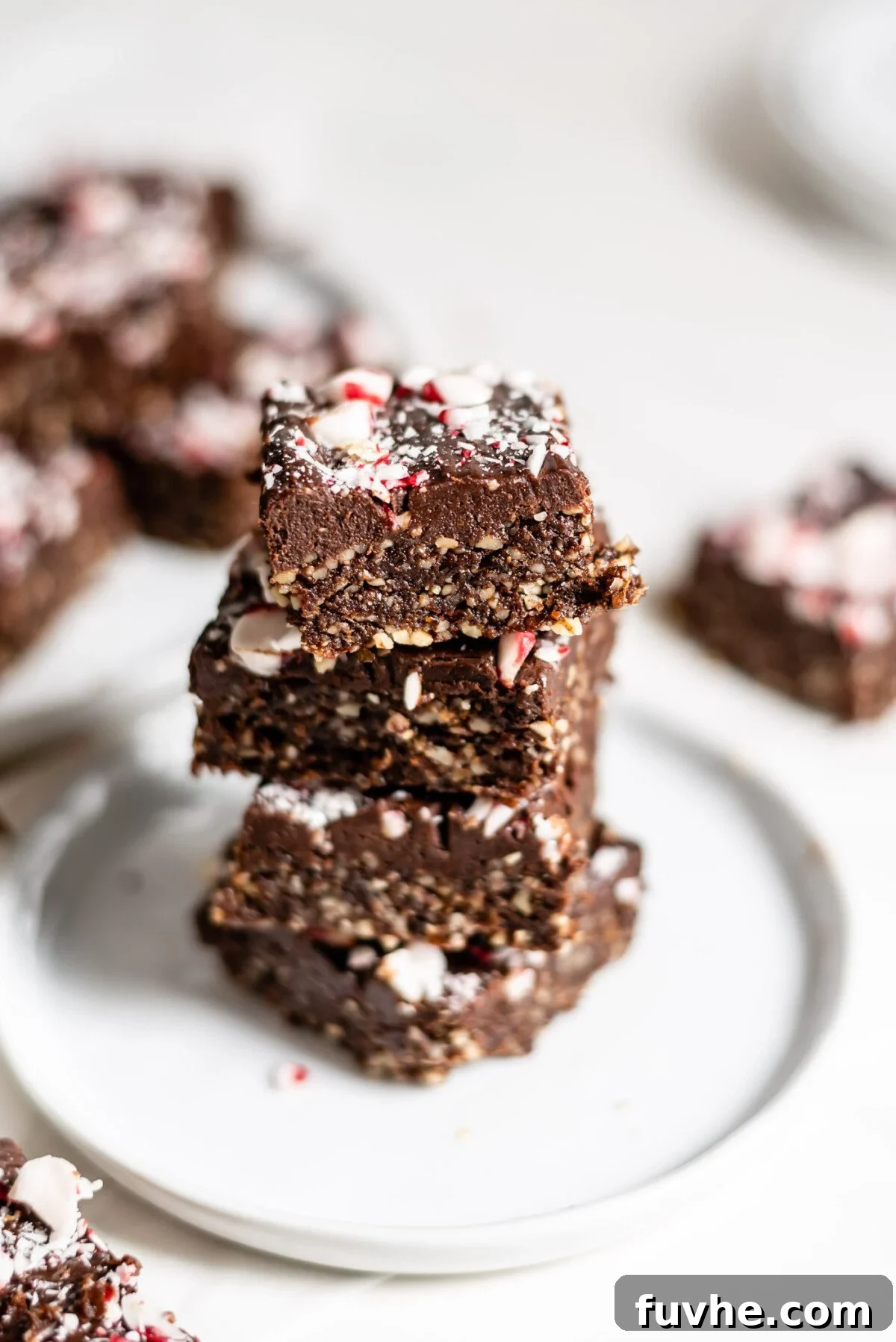Stack of 4 peppermint brownies topped with crushed candy canes on a small plate, ready to be eaten.