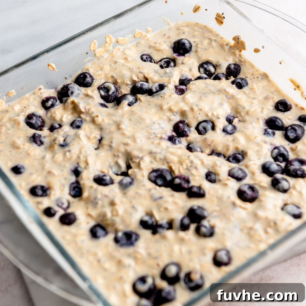 Protein-Packed Baked Oats 7 Raw protein baked oatmeal mixture with fresh blueberries on top, in a glass baking dish before baking.