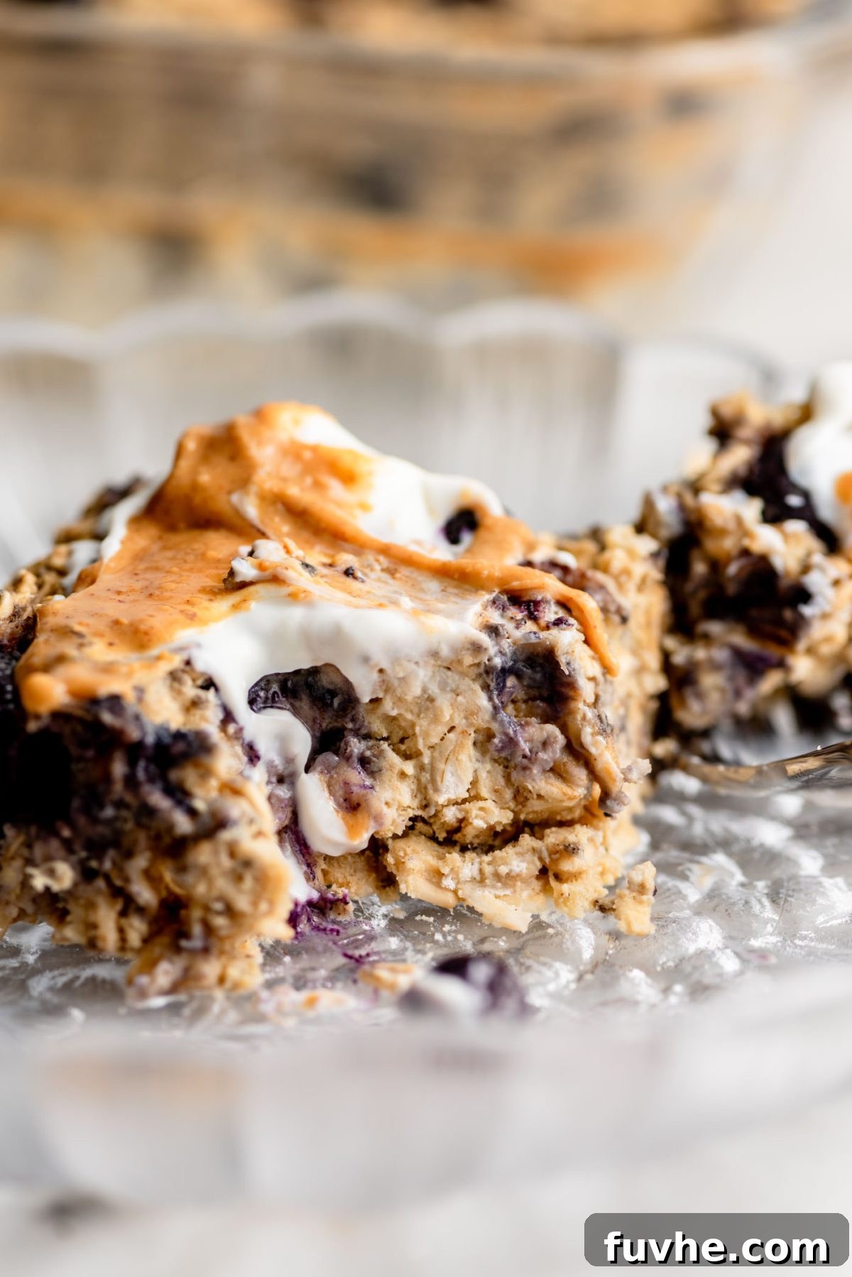 Protein-Packed Baked Oats 9 A square serving of protein baked oatmeal topped with a creamy swirl of peanut butter and a scoop of Greek yogurt on a glass plate.