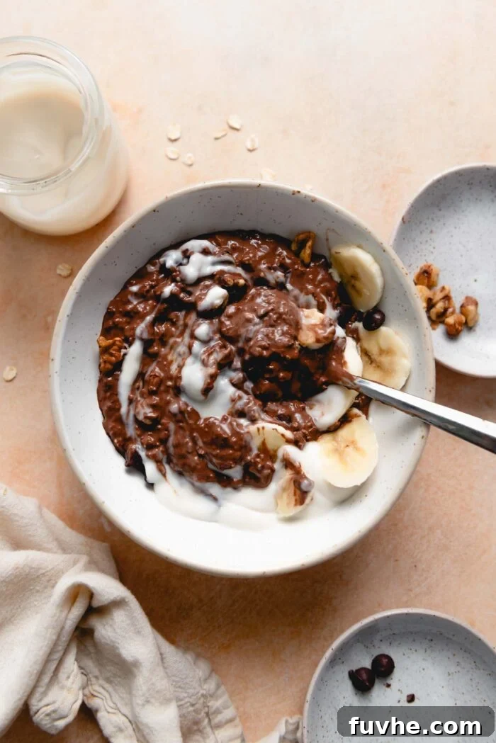 Bowl of chocolate oatmeal topped with sliced banana, nuts and yogurt.