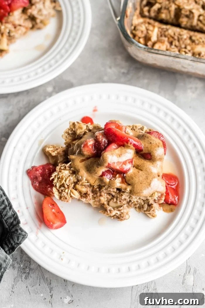 A portion of baked apple cinnamon oatmeal on a plate topped with almond butter and strawberries, showcasing its delicious appeal.