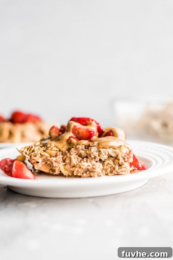 A square of apple baked oatmeal topped with almond butter and strawberries on a plate, ready to be enjoyed.
