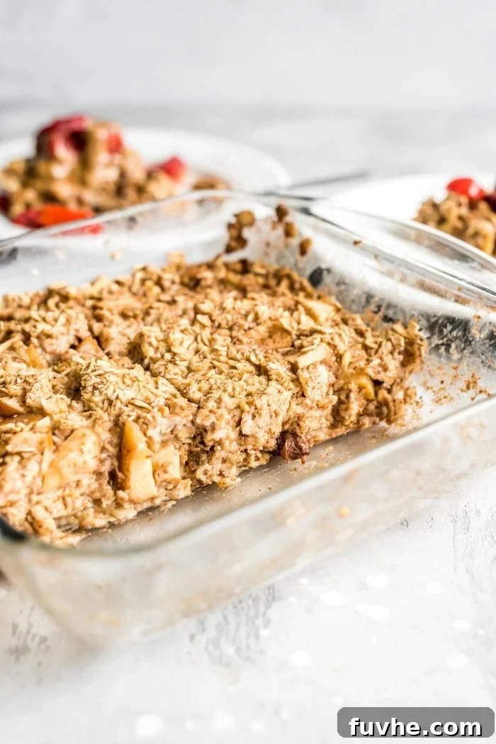 Apple cinnamon baked oatmeal in a glass baking dish with two portions removed and on plates in the background, ready to be served.