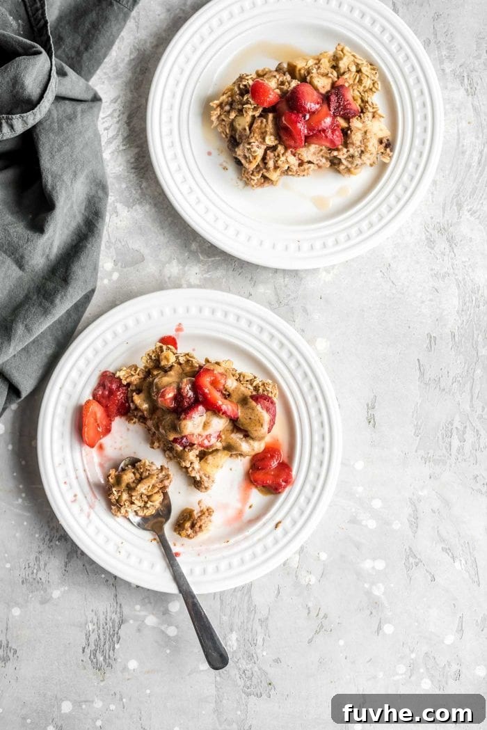 Two plates of apple baked oatmeal topped with sliced strawberries and peanut butter. One plate has a fork on it, ready to be eaten.