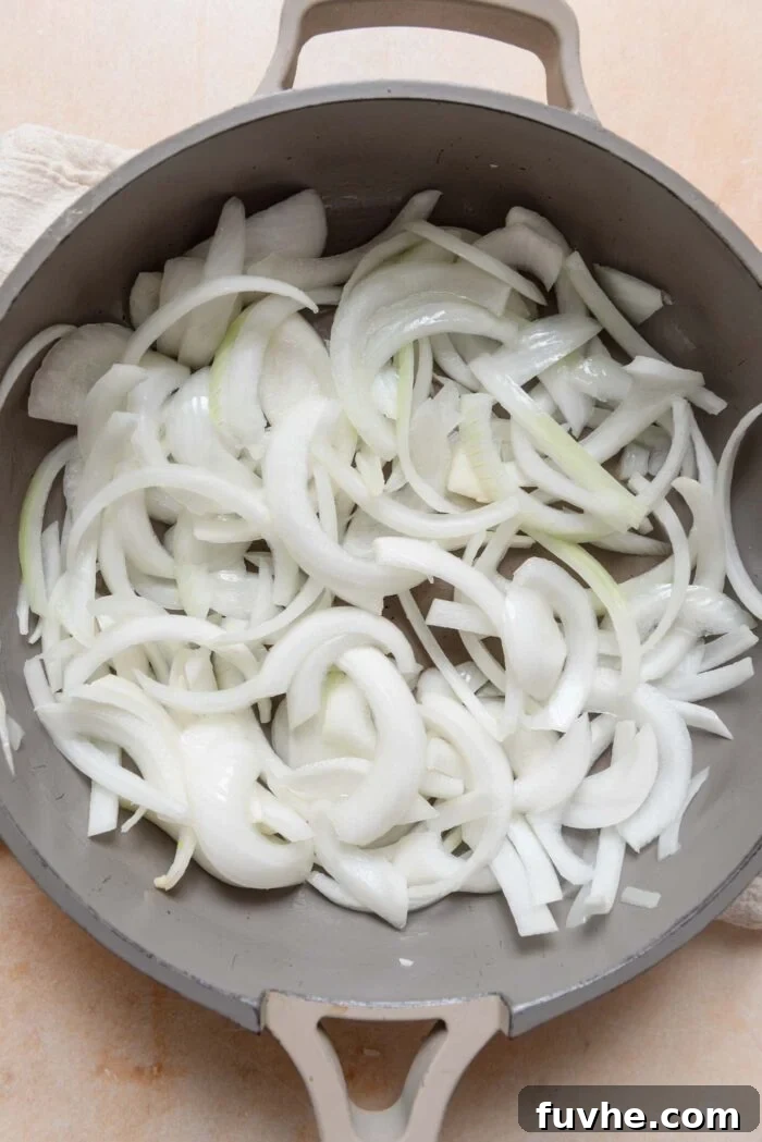 Finely sliced onions gently cooking in a large skillet, creating a fragrant base for the curry.