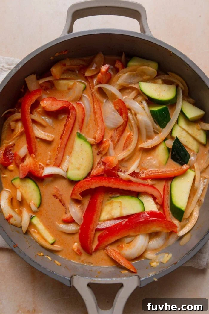 A simmering pan of red curry, rich with colorful vegetables like bell pepper and zucchini, bathed in a creamy coconut sauce.