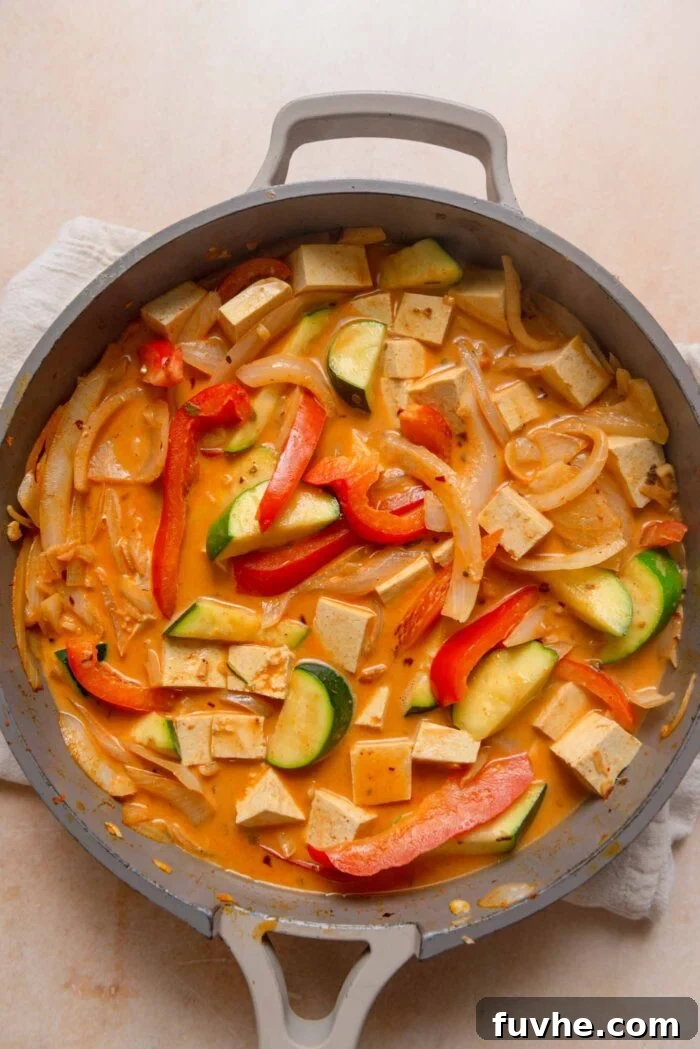 Cubed tofu being added to the simmering red curry, alongside fresh lime juice and chili flakes for seasoning.