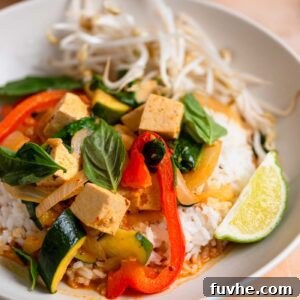 A beautifully presented bowl of vegan Thai red curry with tofu and vegetables, garnished with fresh bean sprouts, basil, and a lime wedge, ready to be enjoyed.