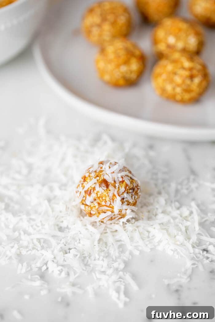Spiced Carrot Cake Fuel Bites 6 An energy ball being rolled in shredded coconut on a counter top.