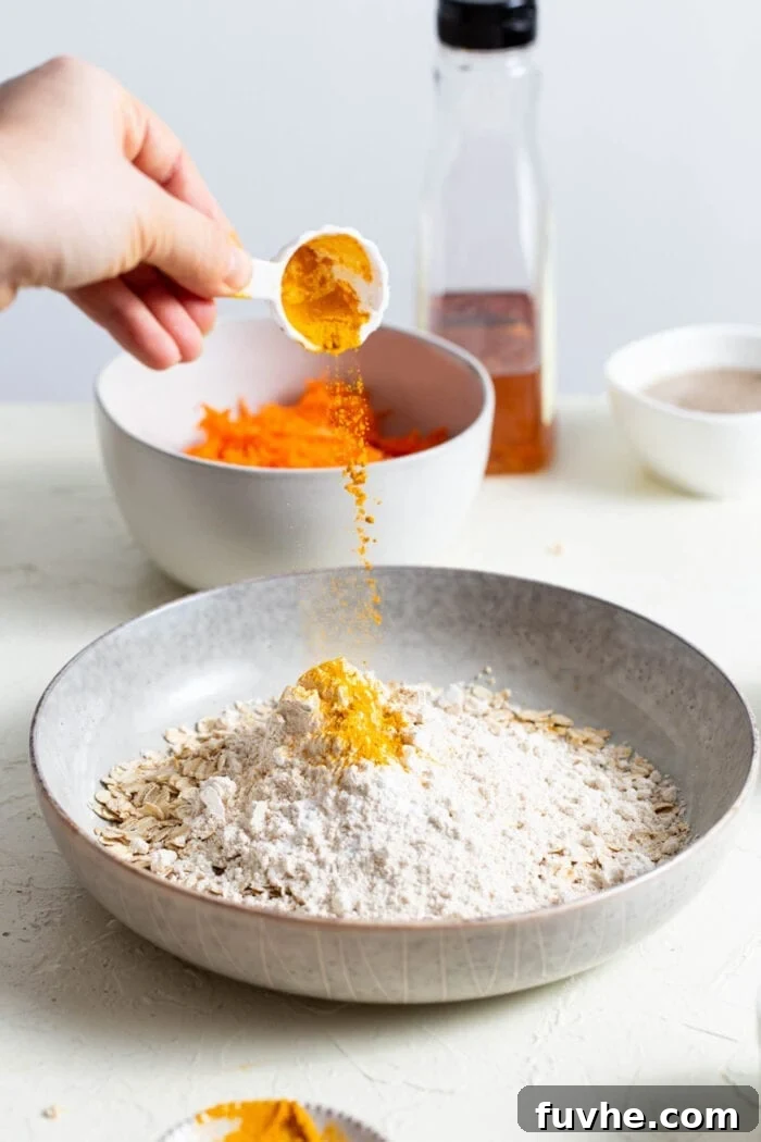 Adding ground turmeric to a mixing bowl filled with oats and other dry ingredients.