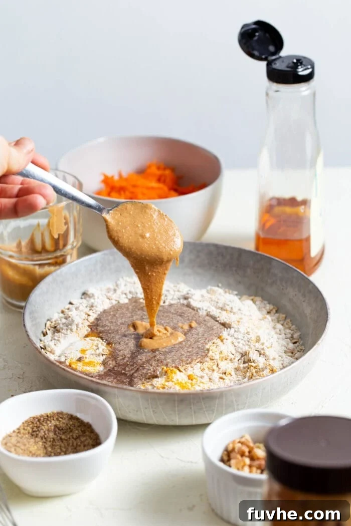 Pouring creamy natural peanut butter into a mixing bowl with other wet ingredients.