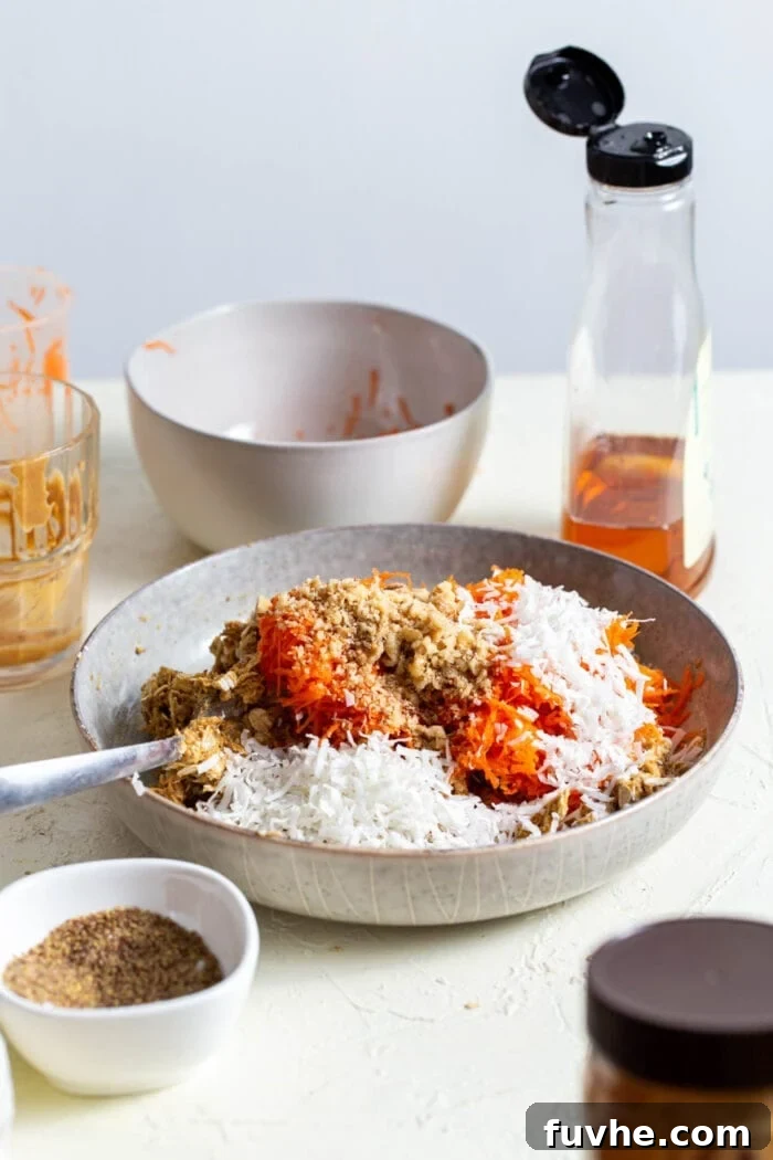 A mixing bowl with shredded carrots, walnut pieces, and coconut being folded into cookie dough.