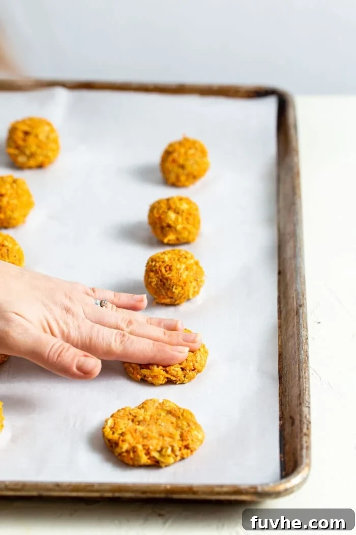 Pressing balls of vegan cookie dough into cookie shapes on a baking pan lined with parchment paper.