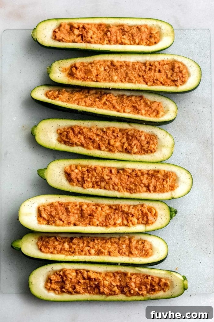 Chickpea stuffed zucchini boats ready to go in the oven on a baking tray lined with parchment paper.