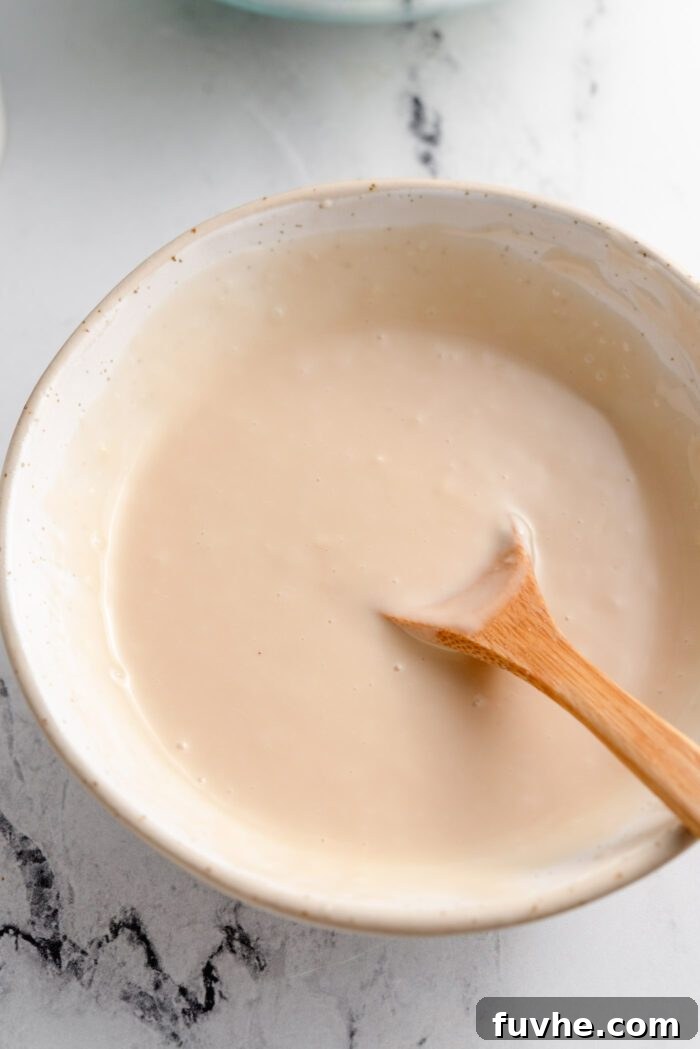 A creamy broccoli salad dressing made with mayo in a small bowl. A small wooden spoon rests in the bowl.