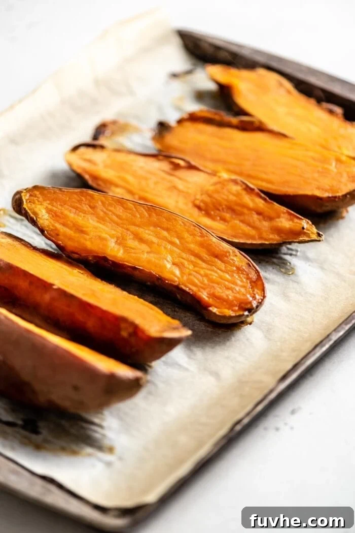 6 baked sweet potato halves on a baking tray lined with parchment paper.