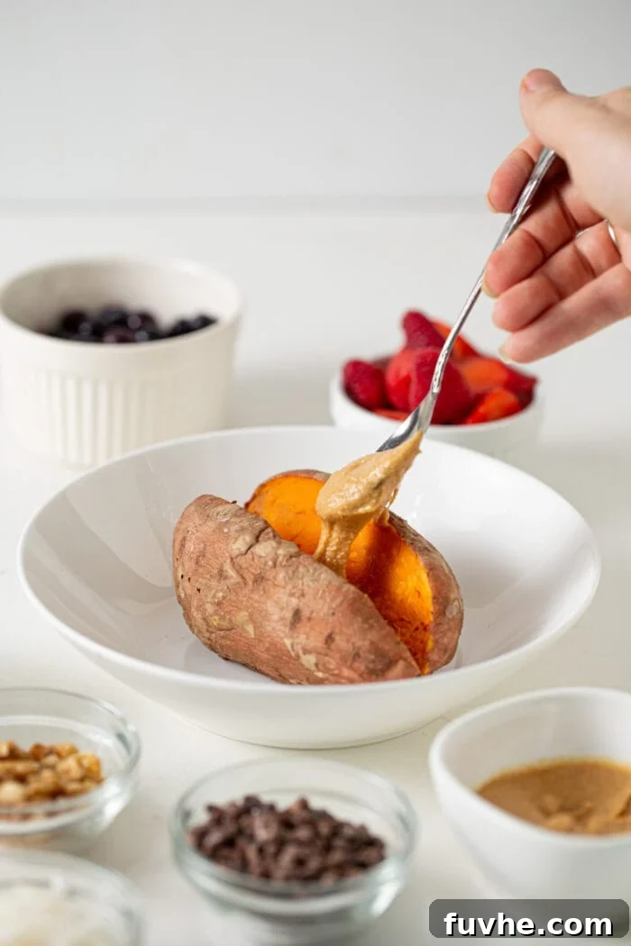 Hand adding a spoonful of peanut butter to a baked sweet potato in a bowl.