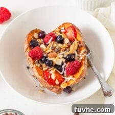 Close up of a baked sweet potato in a bowl topped with berries, almonds, peanut butter and coconut.