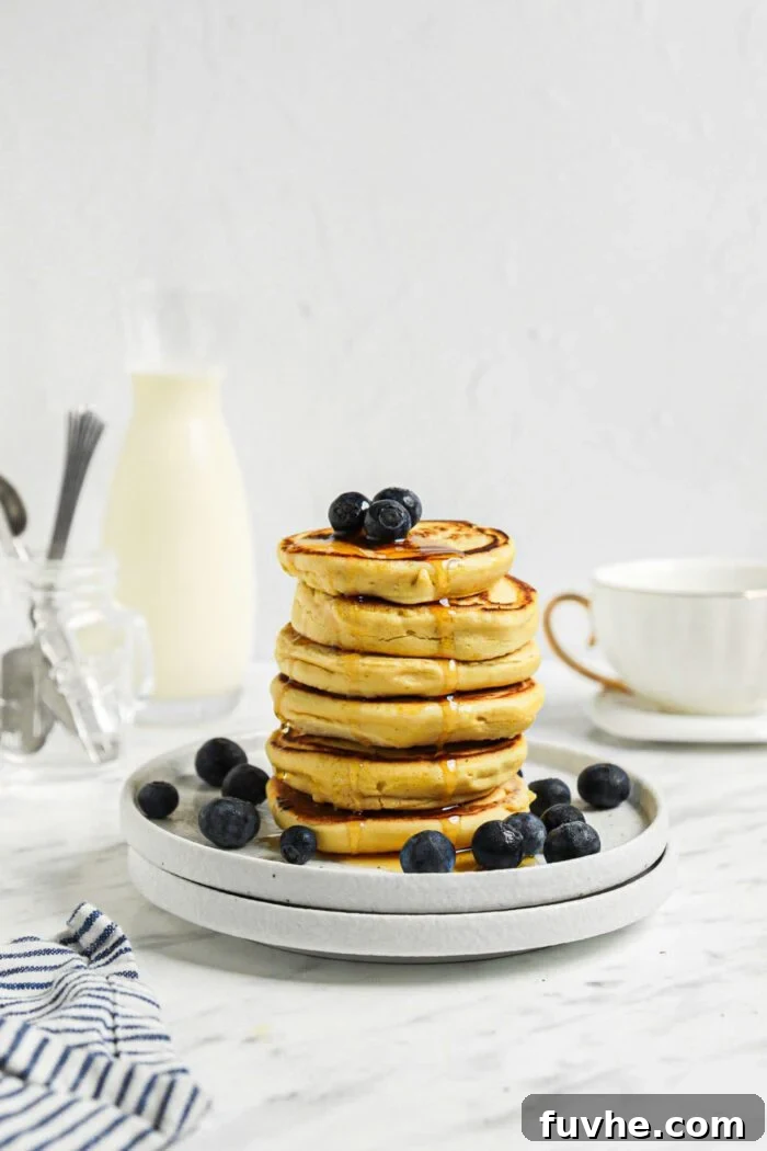 Stack of 6 thick chickpea flour pancakes topped with blueberries and maple syrup on a small plate.