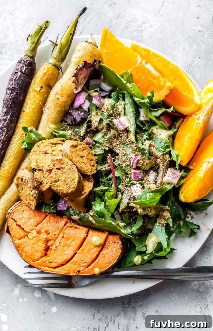 A plate with sweet potato, orange, salad, vegan sausage and roasted carrots.