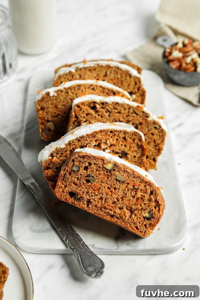 Sliced vegan carrot cake banana bread topped with cream cheese frosting on a marble cutting board.