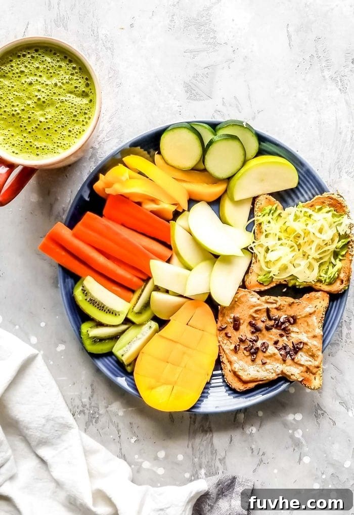 Two pieces of toast with almond butter and sauerkraut, a piece of mango, slices of kiwi and papaya, apple slices and raw zucchini slices of a plate.