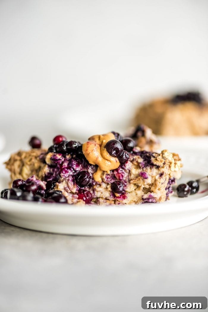 Banana baked oatmeal on a small white plate topped with berries and peanut butter.