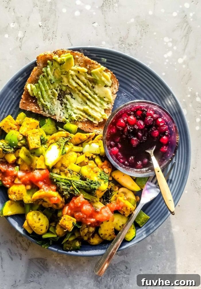 A plate of tofu scramble with a piece of avocado toast and some berries.