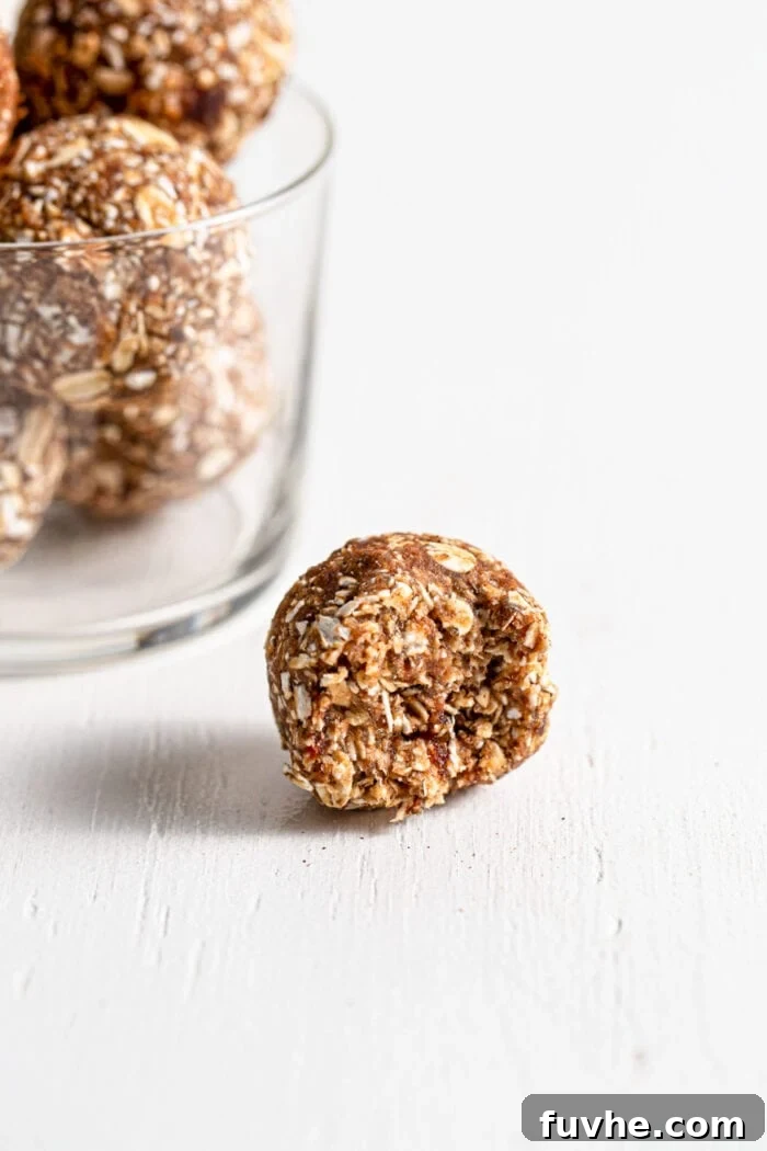 Warm Spice Energy Drops 8 Close-up of a single cinnamon energy ball, showcasing its texture, with a jar of more energy balls blurred in the background.