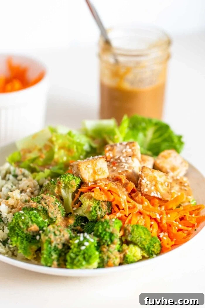 A bowl with carrot, tofu, broccoli, cauliflower rice, tofu and peanut sauce.