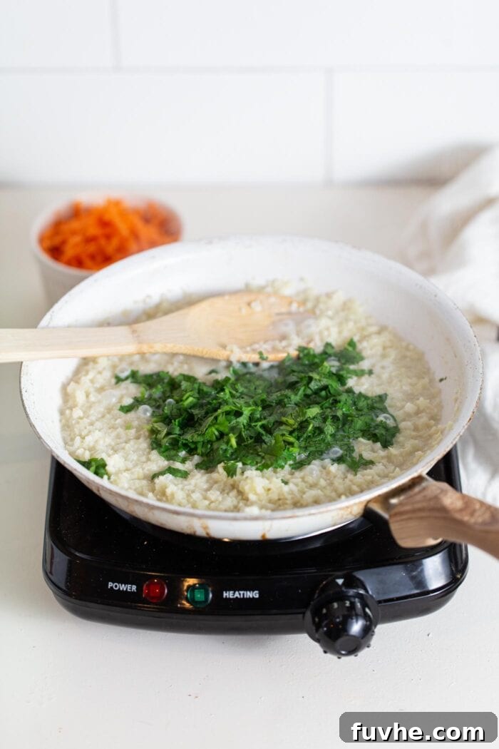 Cauliflower rice in a skillet with cilantro being stirred in.