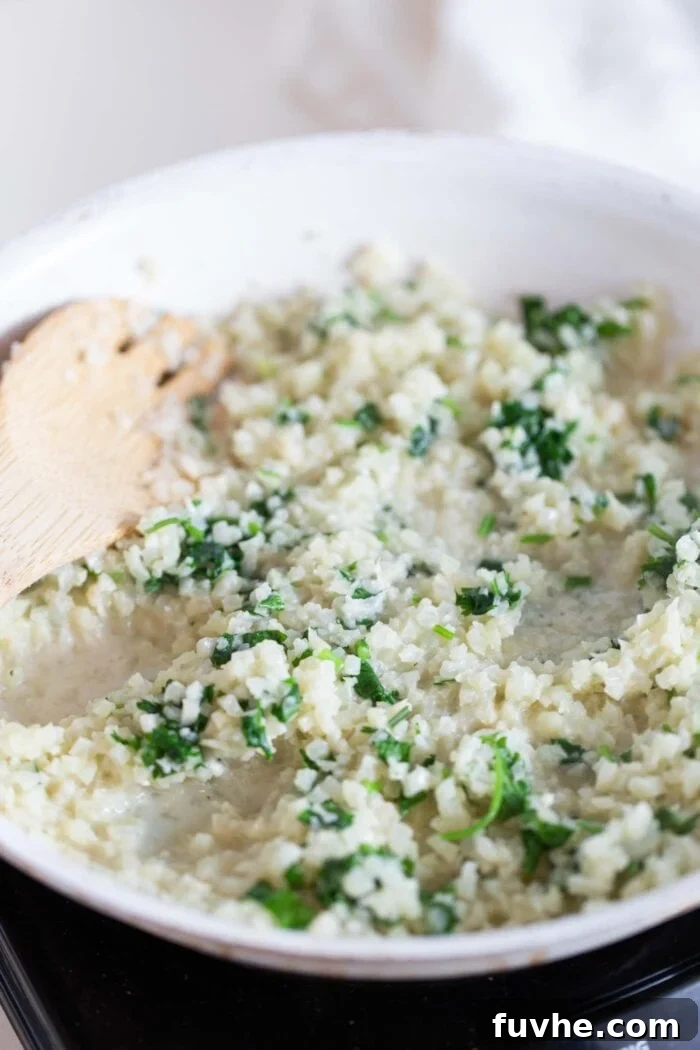 Cauliflower rice in a skillet with cilantro and a wooden spoon.