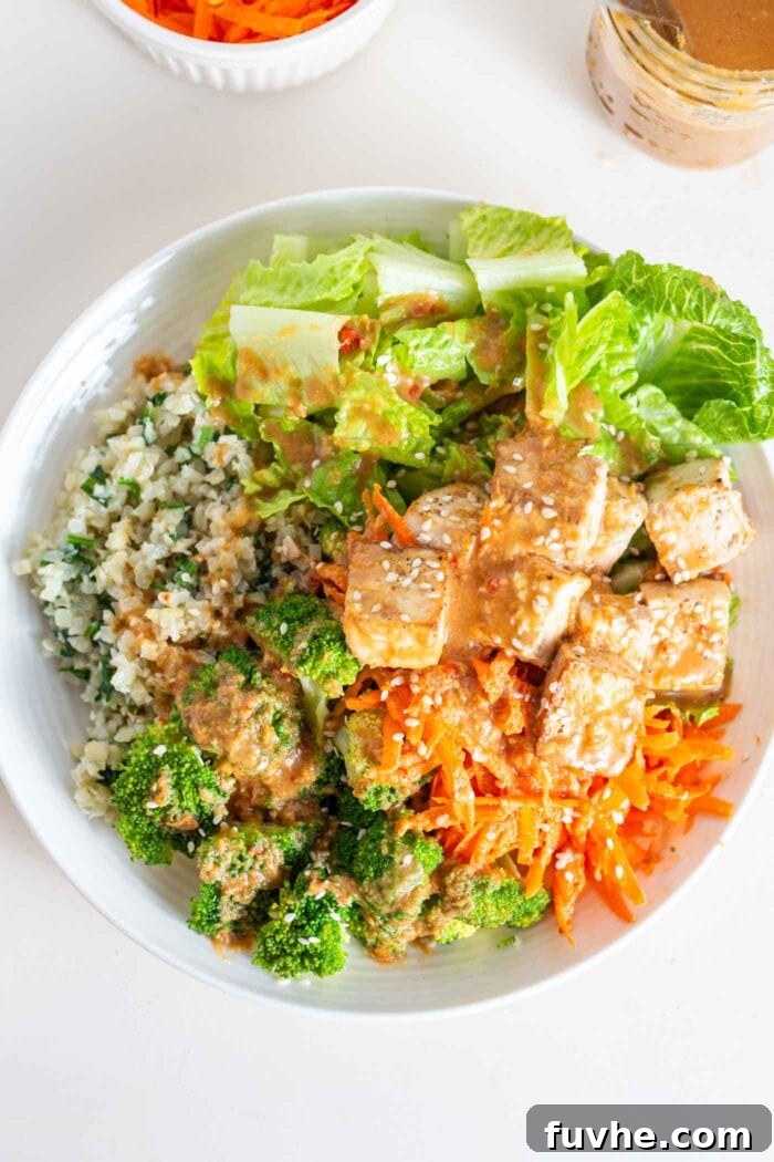 A overhead image of a bowl with carrot, tofu, broccoli, cauliflower rice, tofu and peanut sauce.