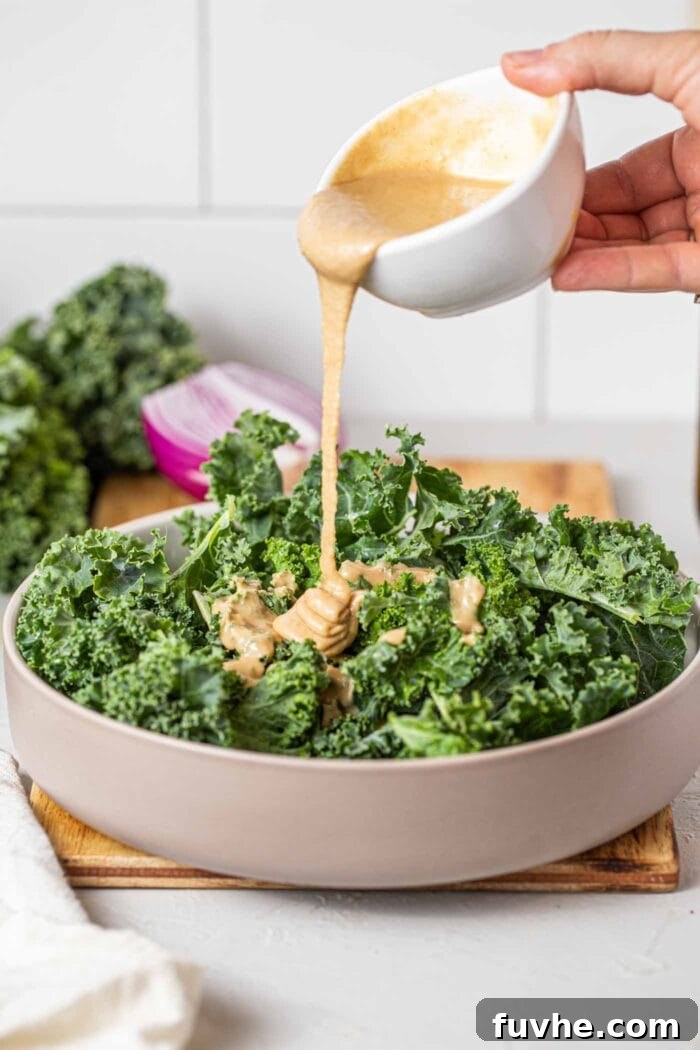 Crispy Buffalo Cauliflower Kale Salad 7 A rustic ceramic bowl filled with freshly chopped kale, being generously drizzled with a creamy tahini dressing, preparing it for the salad.