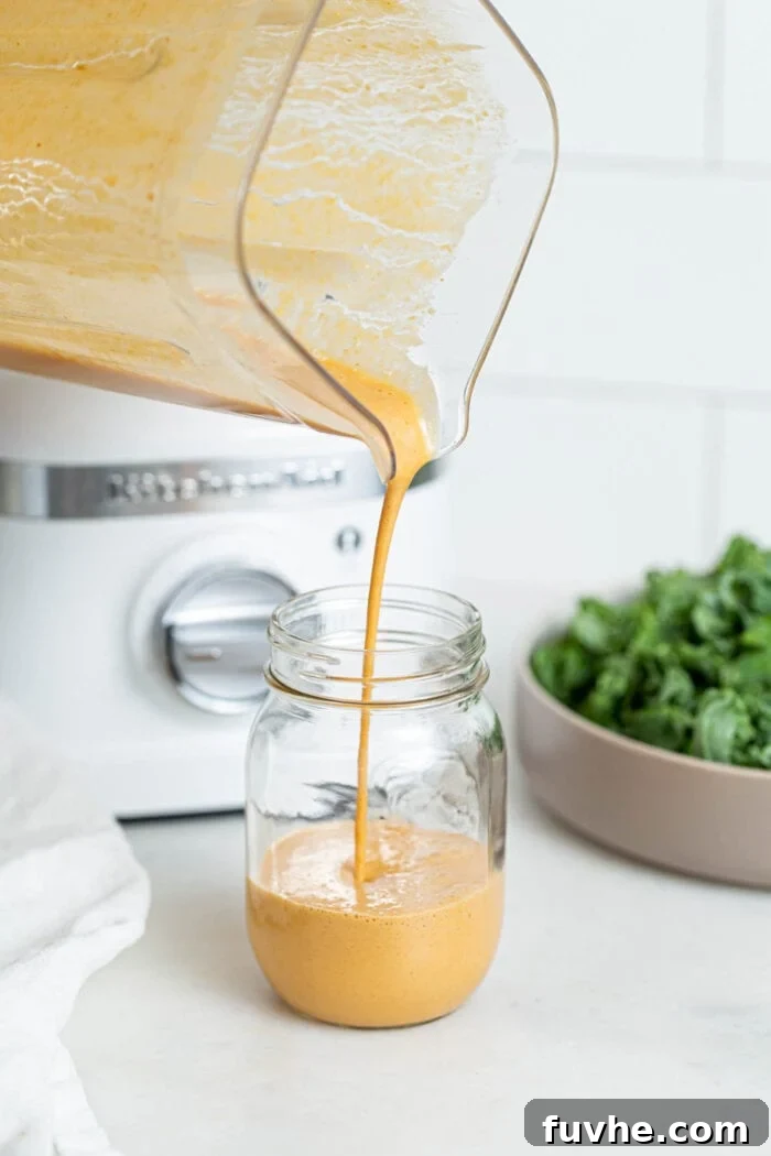 Pouring peanut sauce from a blender into a glass jar.