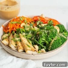 A bowl of tofu and fresh veggies on a counter with a jar of sauce in background.