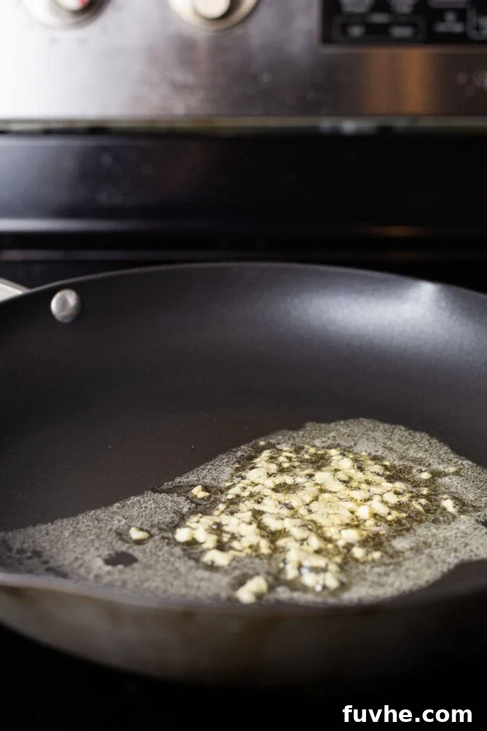 Silky Vegan Pumpkin Pasta 4 Garlic being sautéed in melted butter in a cast iron skillet on the stovetop.