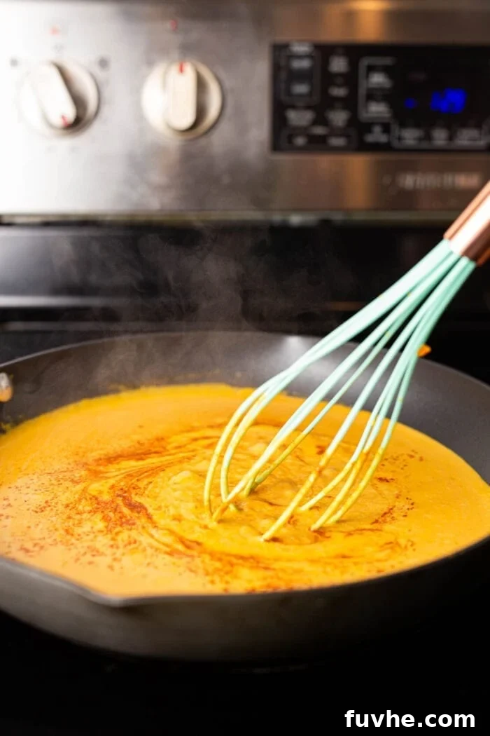 Silky Vegan Pumpkin Pasta 5 Creamy pumpkin pasta sauce being stirred with a whisk a skillet on the stovetop.