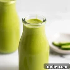 Two jars of creamy green mango pineapple smoothie with a few pieces of spinach scattered around them.
