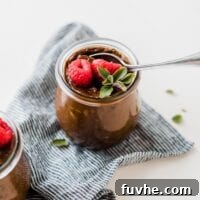 Small glass jar of vegan chocolate avocado pudding topped with raspberries and mint.