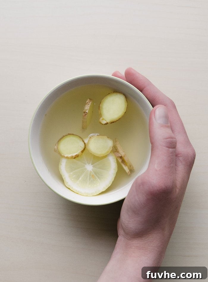 Rise and Shine Inflammation Free 8 Hand cupping a mug of tea with ginger and lemon in it.