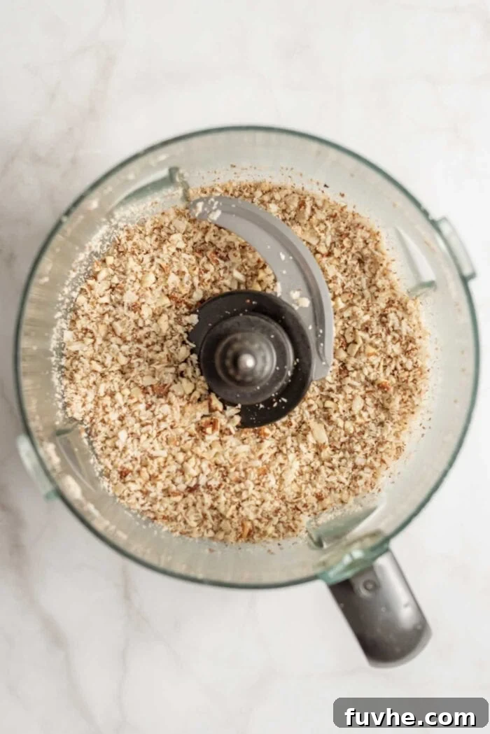 Crumbly blend of coconut, almonds, and pumpkin pie spice in a food processor, ready for the next step.