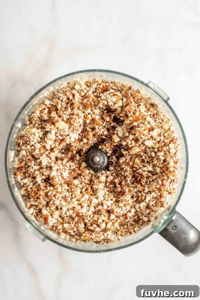 Dates, coconut, and almonds blended into a thick, sticky dough in a food processor, showcasing the perfect binding consistency.
