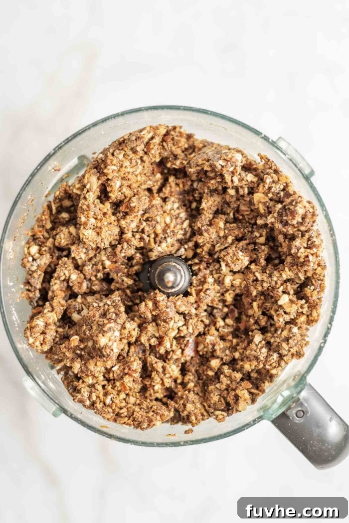 Thick, sticky, raw energy bar dough in a food processor, demonstrating the final blended consistency before pressing.