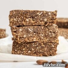 Stack of 3 energy bars on parchment paper with some almonds in the foreground.