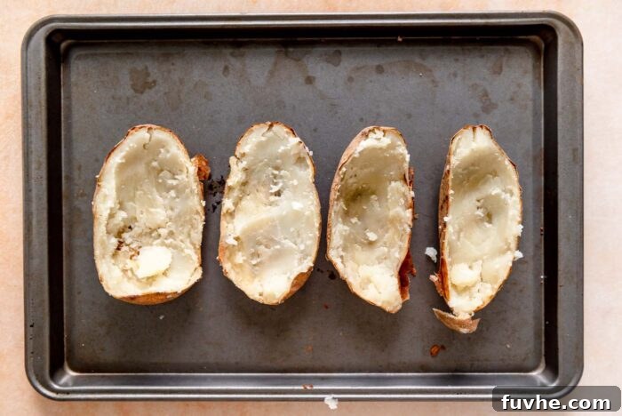 Four potato skins, expertly scooped out with the fluffy potato flesh removed, neatly arranged on a baking sheet, ready for the delicious filling.
