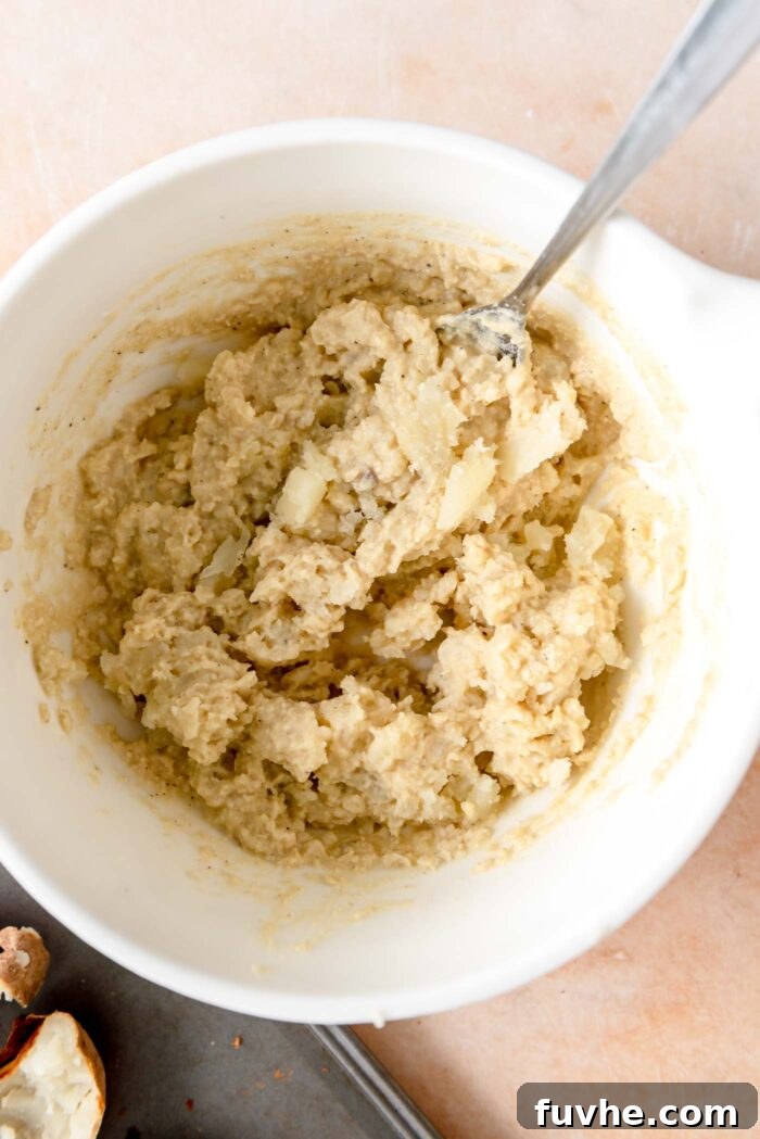 Mashed potato flesh expertly mixed with creamy cashew sauce, resting in a large mixing bowl with a spoon, showcasing a perfectly combined filling.