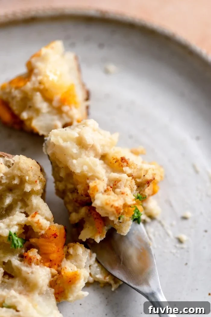 A close-up of a fork holding a scoop of creamy vegan twice-baked potato filling, resting on a white plate, ready for a delicious bite.