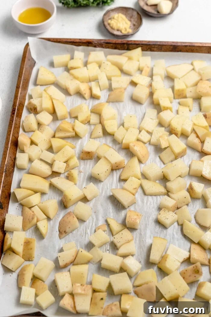Cubed russet potatoes on a separate baking tray lined with parchment paper, seasoned and ready for roasting.