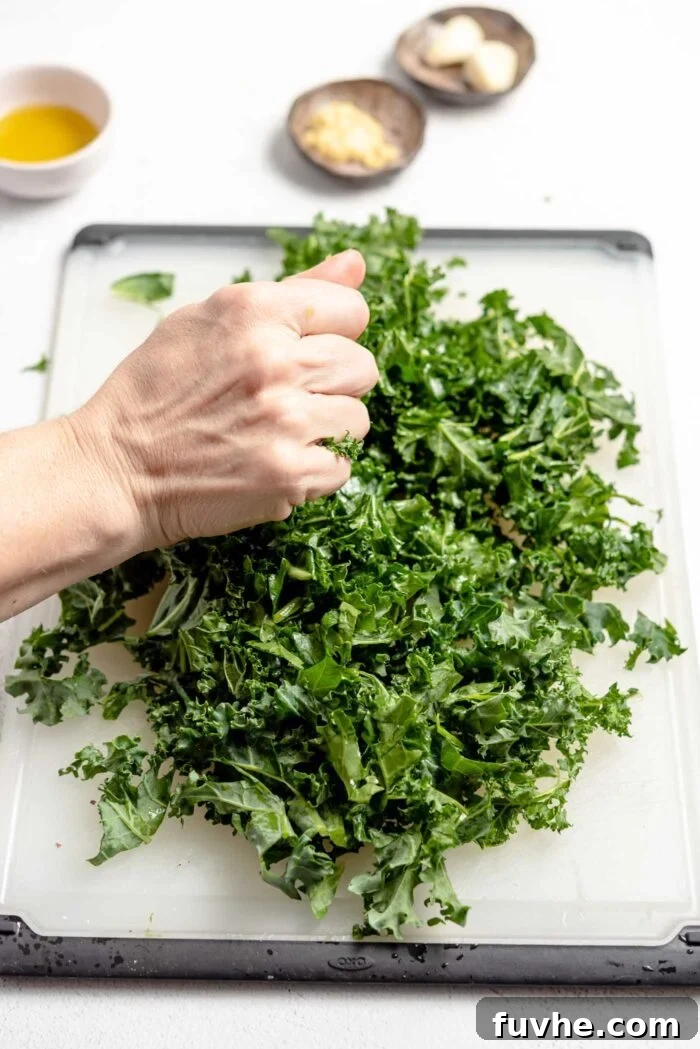 A hand gently squeezing and massaging a pile of chopped kale on a cutting board to soften its texture.